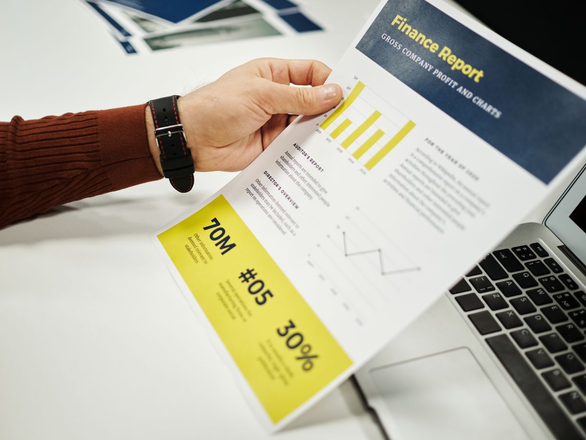 Pessoa analisando relatório financeiro com gráficos na mesa.
